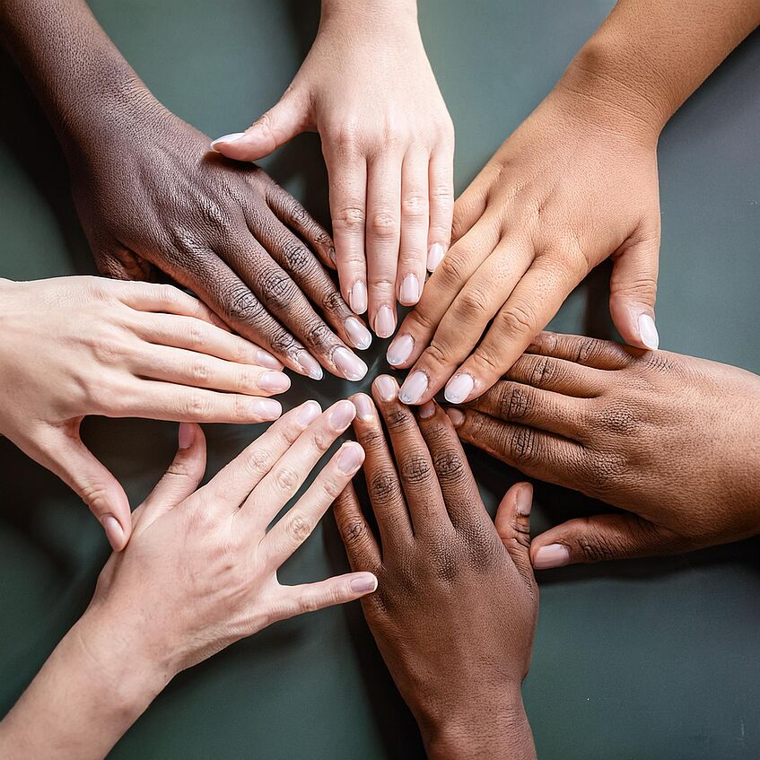 Different people putting their hands together in a circle to show team spirit.