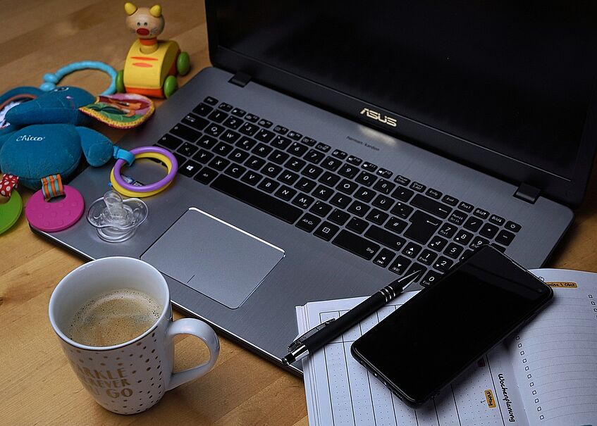 A laptop surrounded by tools for working but also childrens toys.